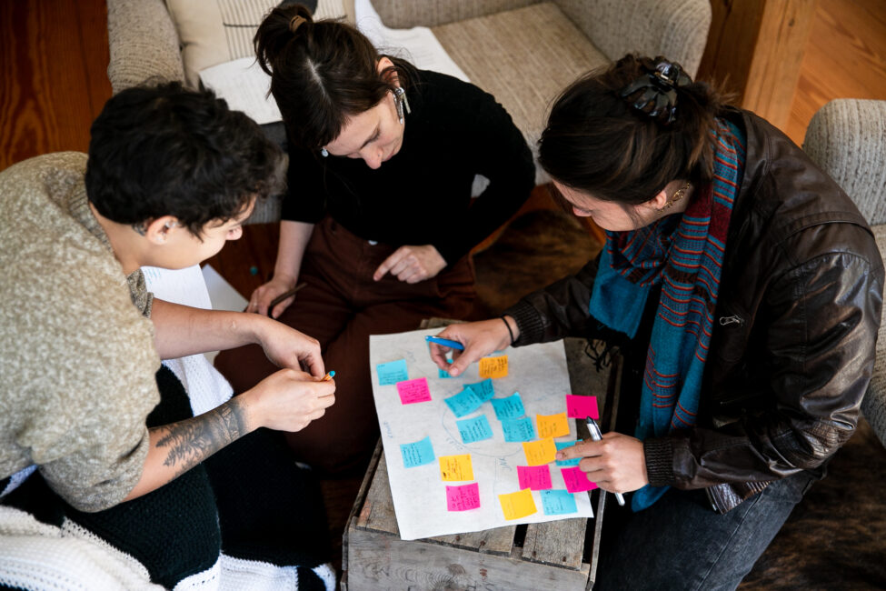 Three people sitting together on the ground, adding sticky notes to a sheet of paper.